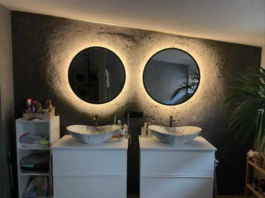 Fugenloses Bad mit Betonoptik-Wand und zwei beleuchteten Rundspiegeln