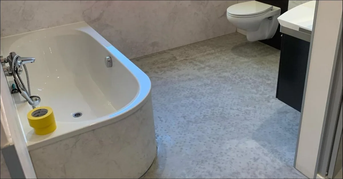 Fugenloses Bad: Badewanne mit Verkleidung und Wand in heller Marmoroptik, Boden in Betonoptik