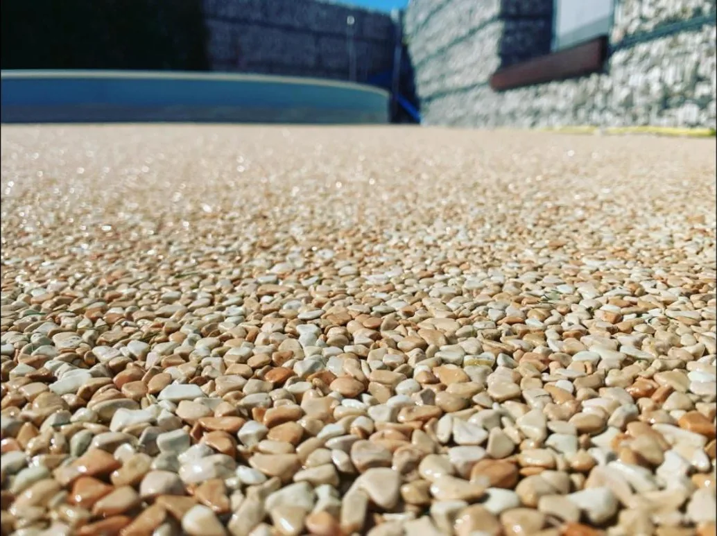 Steinteppich aus Marmorkieseln auf einer Terrasse am Pool vor einer Gabionenwand